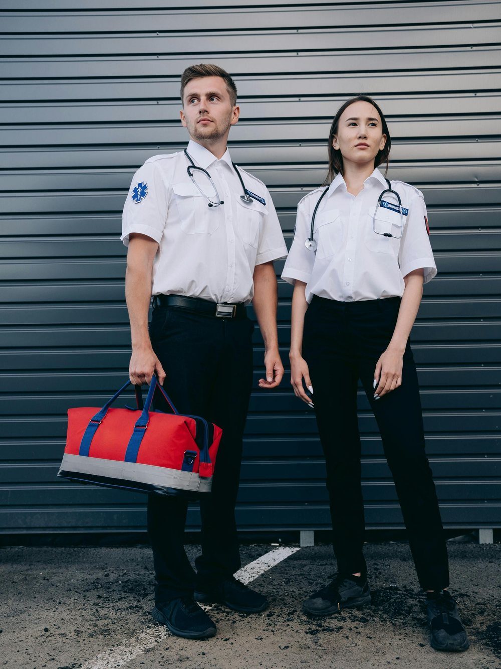Two paramedics standing ready with a medical response bag